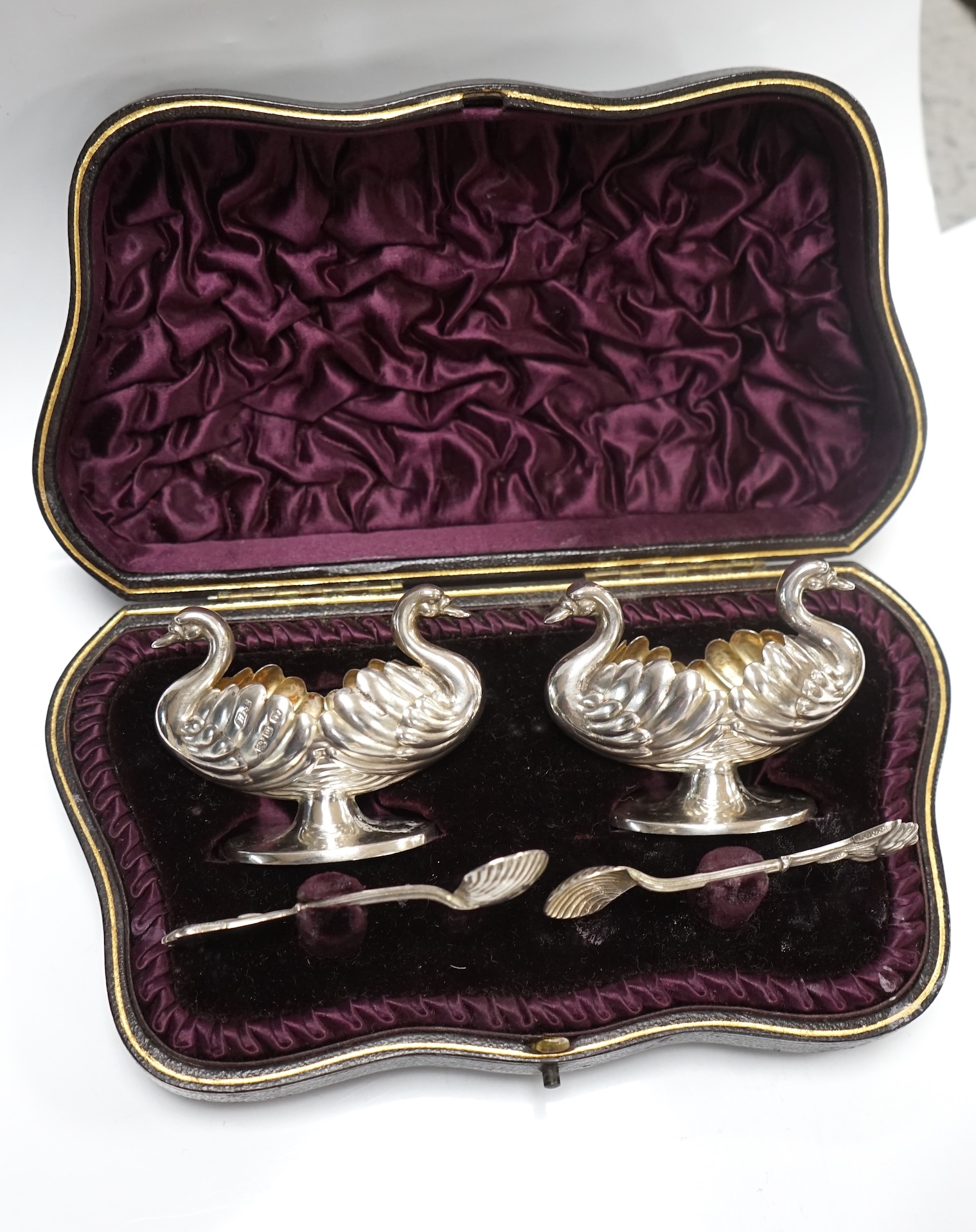 A cased pair of silver double headed swan shaped salts and spoons, Hilliard & Thomasson, Birmingham, 1896, a pair of later silver mounted dwarf candlesticks and a plated butter shell. Condition - fair